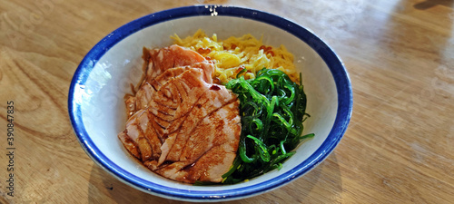 Japanese rice bowl filled with salmon, sliced sweet egg slice and seaweeds on wooden table. photo