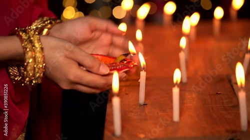 Hindu Woman Illuminating A Diya Lamp. Indian housewife or newly wed bride wearing traditional woman wear & gold jewelry, lighting a clay diya or oil lamp from a lit candle at a temple on Diwali night.