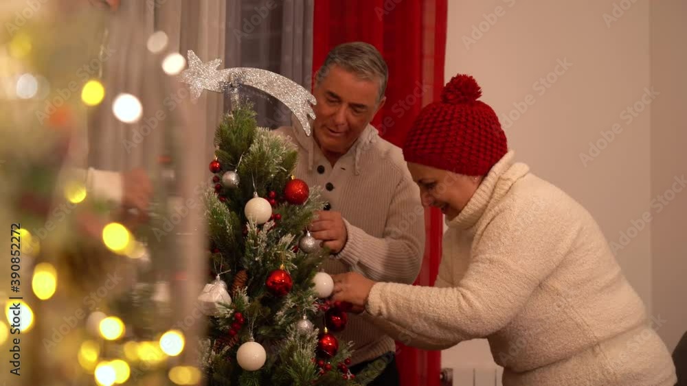 Man and woman working together decorating christmas tree at home with red and white balls Man and woman working together decorating christmas tree at home with red and white balls