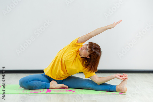 An adult woman doing yoga in a white hall. Beautiful woman doing stretching.