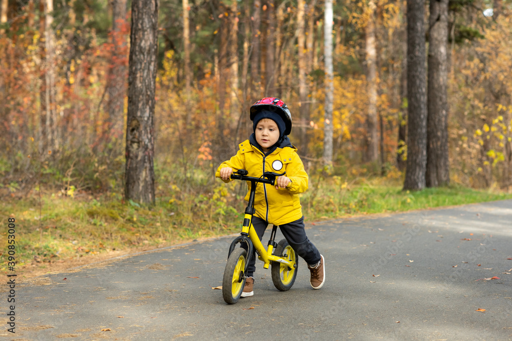 Cute little boy in yellow jacket and protective helmet riding on balance bicycle Cute little boy in yellow jacket and protective helmet riding on balance bicycle