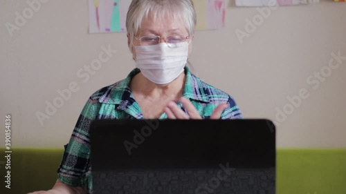 Older woman in protective medical mask at a laptop. Woman talking on the Internet during quarantine