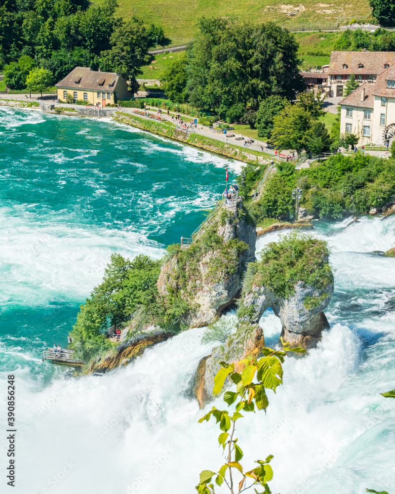 Panorama des cascades du Rhin ou Rheinfall en Suisse par une journée ensoleillée avec un ciel bleu avec les rochers et un village et les embruns du fleuve.