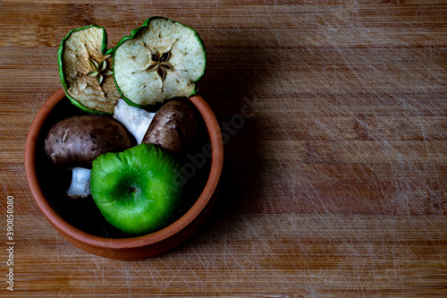 Green dried apple slices and dried mushrooms in brown plate on the brown wooden background 