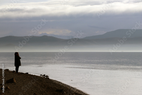 Loneliness concept, fog, lonely woman looks at the sea against the background of mountains.