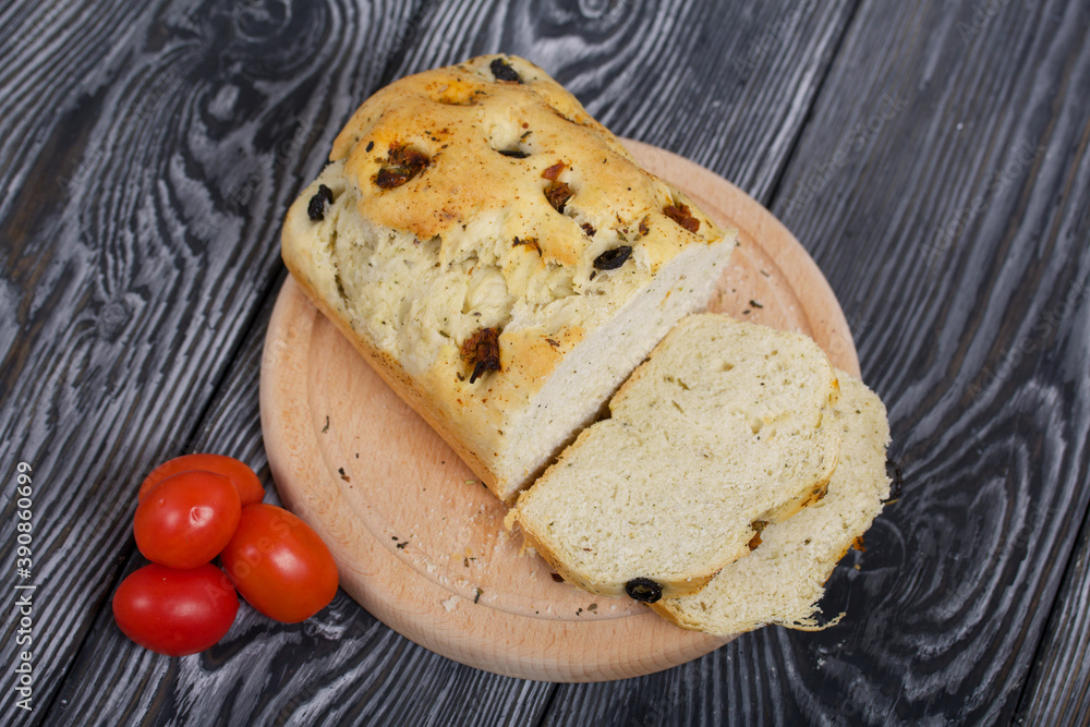 Focaccia bread with olives and sun-dried tomatoes. Several red tomatoes are nearby. On pine boards. Focaccia bread with olives and sun-dried tomatoes. Several red tomatoes are nearby. On pine boards.
