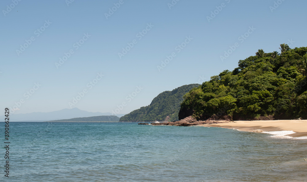 Beautiful landscape of a beach in the mexican pacific coast in a sunny day with trees, palms and green hills, some waves and cliffs with rocks