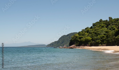 Beautiful landscape of a beach in the mexican pacific coast in a sunny day with trees, palms and green hills, some waves and cliffs with rocks