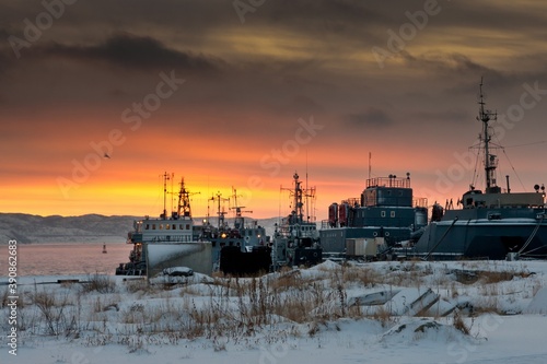 Moored ships in dock of Barents Sea and the ground covered with snow and faded grass in winter in Severomorsk, Russia. photo