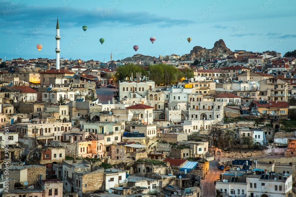 Old stone houses of Ortahisar in Cappadocia with tower in the middle at sunrise. Hot air balloons are on the background. Turkey.