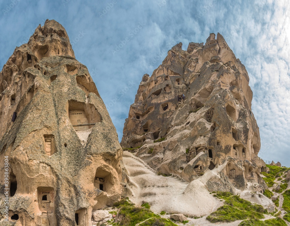 Uchhisar Castle against blue sky. It's a large rock formation rising tall like a giant anthill full of small holes. It attracts visitors with its intriguing history. Cappadocia. Turkey.