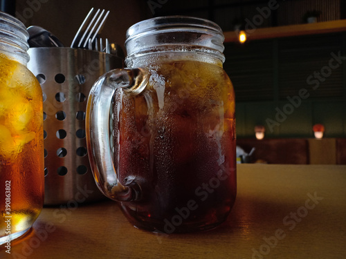 Close up iced tea in a mason jar with ice cubes in it. Put it on the café table next to the spoon and fork stainless mug. Very nice photo and suitable for use as background