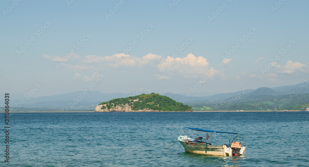 A fishing boat in a mexican beach of the pacific coast with and island behind in a sunny day with a clear blue sky and some mountains in the background