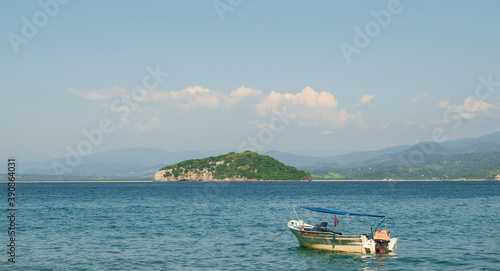 A fishing boat in a mexican beach of the pacific coast with and island behind in a sunny day with a clear blue sky and some mountains in the background © Anthony J.