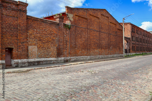 Stone paved historic street and red brick wall against blue sky. Sovetsk, Kaliningrad region