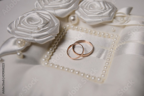 A close-up of two gold rings lying on a white satin pillow. Wedding preparations