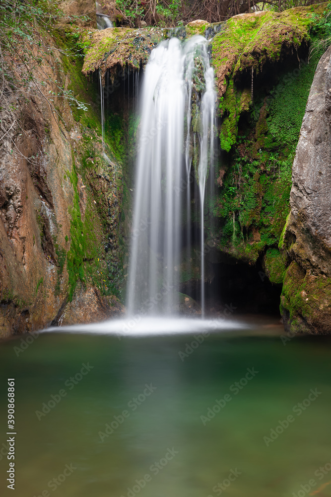 Fototapeta premium Scenic waterfall in rocky canyon, green foreground water with underwater rocks and vivid, colorful moss on the cliffs