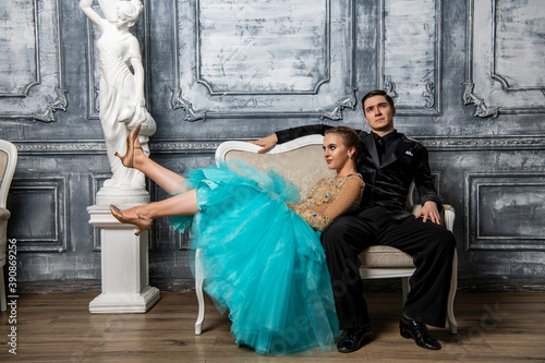 young couple in evening dance costumes posing while sitting on sofa in dance hall © константин константи