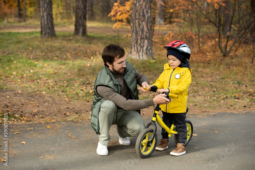 Young father checking balance bike of his son in safety helmet before riding