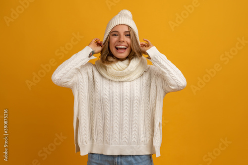 young smiling happy pretty blond woman wearing white knitted sweater, scarf and hat, warm winter cold season fashion accessories trend, posing on yellow studio background isolated © mary_markevich