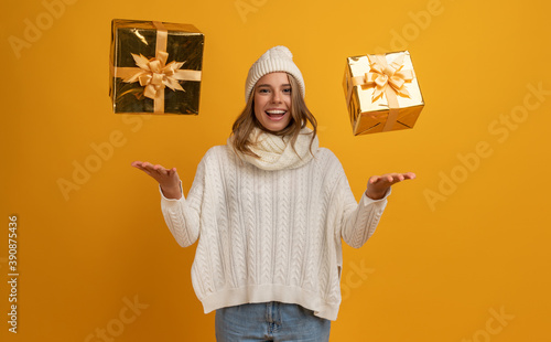 young smiling happy pretty woman with golden present boxes celebrating new year, christmas gifts, wearing white knitted sweater, scarf and hat, winter fashion trend, posing on yellow background