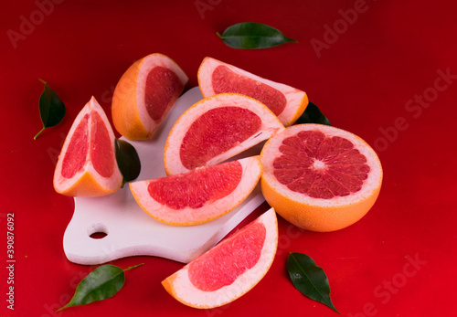 
Sliced ​​grapefruit on a white wooden board on a red background.