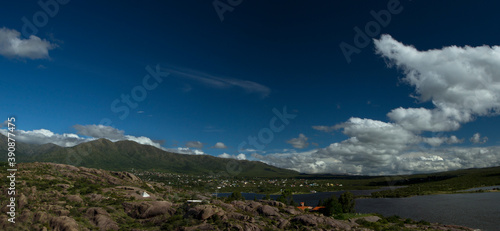Panorama view of El Cajon lake, in Capilla del Monte, Cordoba, Argentina. The pure water lagoon, rocky mountains, green forest and rural town buildings under a deep blue sky in a summer day. 