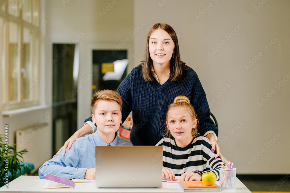 Two happy schoolchild pupils boy and girl woth their tutor working together at lesson in classroom. Female teacher helping explain the task for her two students Two happy schoolchild pupils boy and girl woth their tutor working together at lesson in classroom. Female teacher helping explain the task for her two students