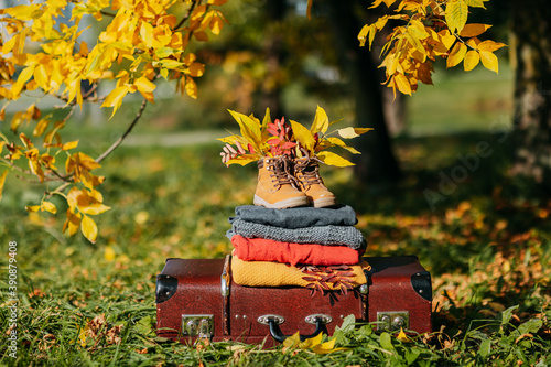 Warm sweater stacks on the vintage suitcase. Knitted sweaters and old boots with foliage inside. Autumn coziness. Black friday sale of sweaters.