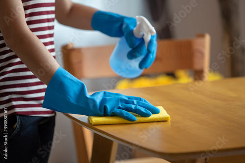 Close up of female housewife hands in rubber gloves holding spray wiping the table in living room at home