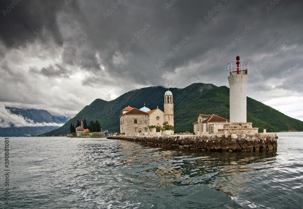 The Church of Our Lady of the Rocks  (Gospa od Skrpjela) and Saint George Benedictine monastery and mountains in clouds in the background in Montenegro. A small artificial island in the sea .