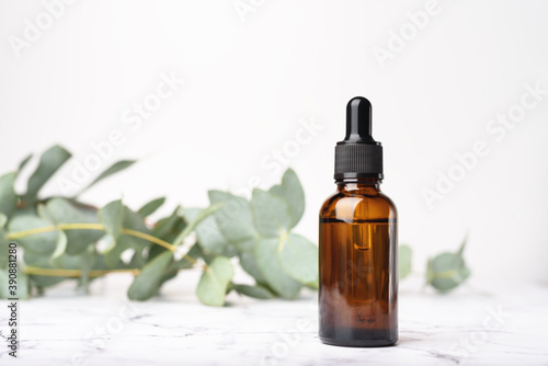 Glass dropper bottles with a pippette with black rubber tip on the beautiful white marble and blurred eucalyptus background. Nature Skin concept. Organic Spa Cosmetics. Trendy concept.