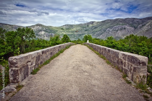 A straight road on the bridge with ramps surrounded with green trees and mountains in the background against cloudy sky in summer in Bosnia and Herzegovina.