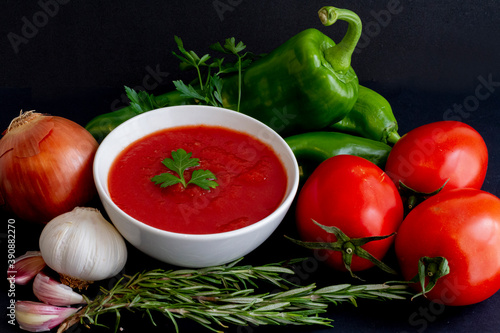 Tomato sauce in a white bowl surrounded by its ingredients: tomato of the "pear" variety, Italian pepper, onion, garlic, rosemary and parsley