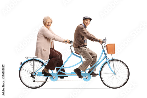 Elderly man and woman riding a blue tandem bicycle and looking at camera