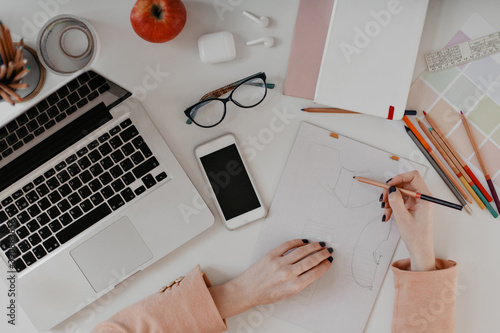 Female hands with black manicure drawing plan at workplace with MacBook, iPhone, glasses and stationary located on it