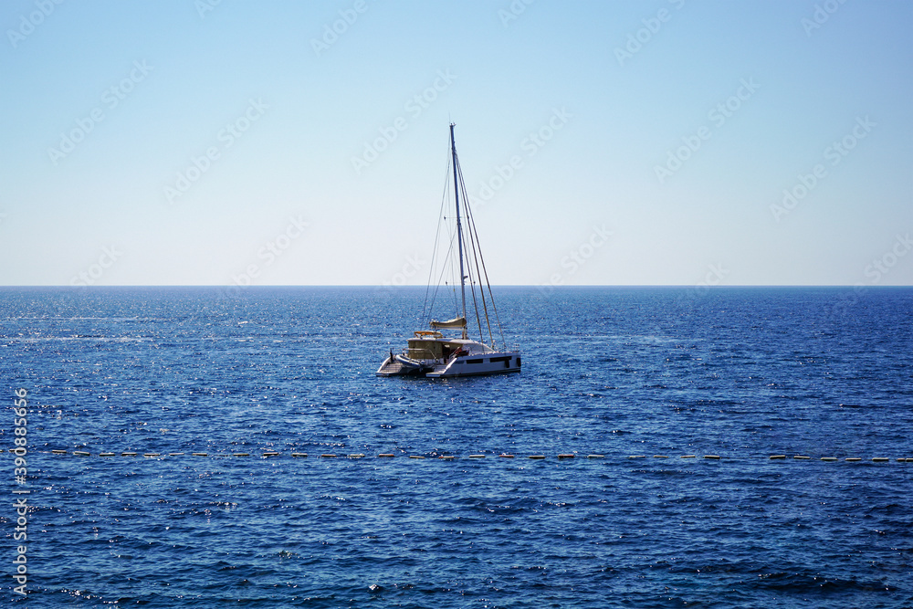 A lone yacht with lowered sails is anchored at sea. Calm sea, sunny day. Rest on a yacht. Sailing. Vacation on a sea yacht. Mediterranean summer landscape. Seasickness. A lone yacht with lowered sails is anchored at sea. Calm sea, sunny day. Rest on a yacht. Sailing. Vacation on a sea yacht. Mediterranean summer landscape. Seasickness.