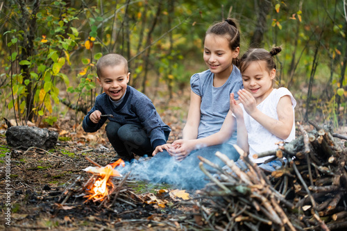 Children sitting near campfire in forest and closing eyes because of smoke