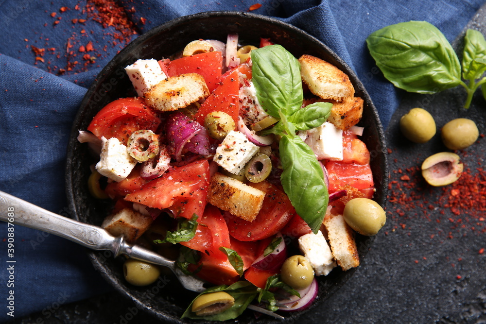 Oriental cuisine. Spicy vegetable salad with spices. Salad of tomatoes, olives, red onions, cheese and basil, croutons on a black cast-iron plate on a black background with red spices. Top view