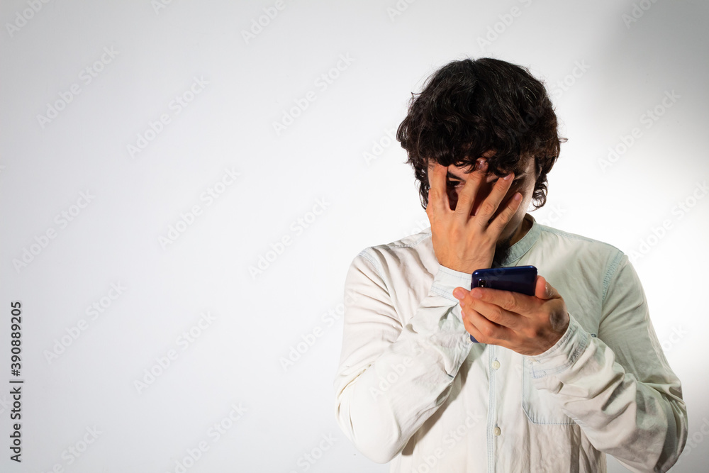 Young hispanic man wearing casual clothes on a white background using a cell phone with angry and worried expression Young hispanic man wearing casual clothes on a white background using a cell phone with angry and worried expression
