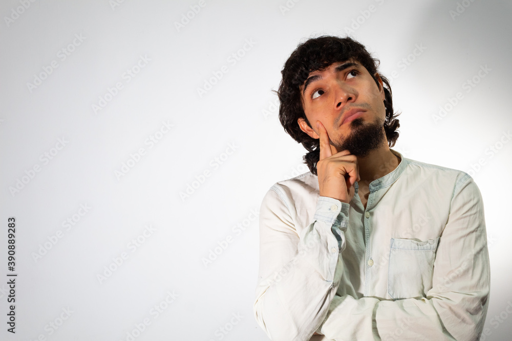 Young Hispanic man wearing casual clothes on a white background with thoughtful and pensive face Young Hispanic man wearing casual clothes on a white background with thoughtful and pensive face