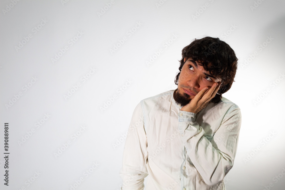 Young Hispanic man wearing casual clothes on a white background with thoughtful and pensive face Young Hispanic man wearing casual clothes on a white background with thoughtful and pensive face