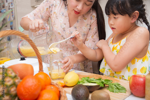 Happy asian family mother and her daughter enjoy prepare freshly squeezed fruits with vegetables for making smoothies for breakfast together in the kitchen.diet and Health concept.