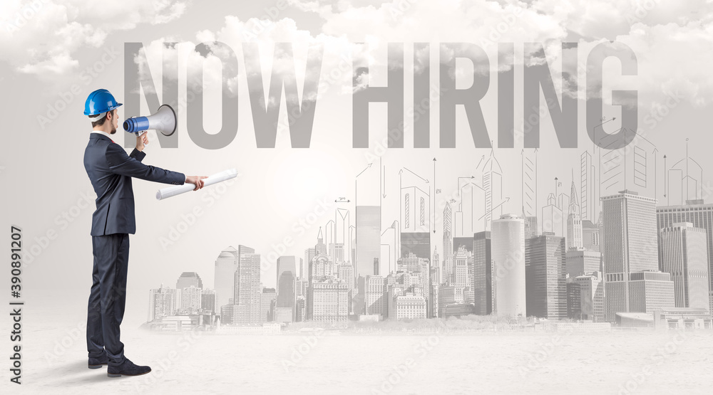 Young businessman with hard hat and NOW HIRING inscription, new business opportunity concept Young businessman with hard hat and NOW HIRING inscription, new business opportunity concept