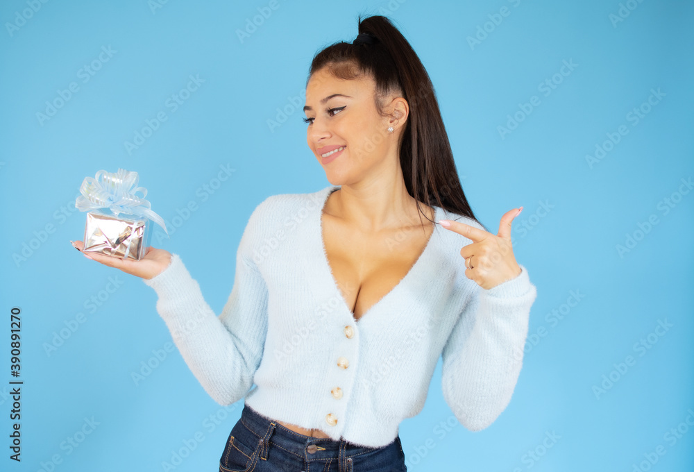 Happy woman showing a small gift box, isolated on blue background Happy woman showing a small gift box, isolated on blue background