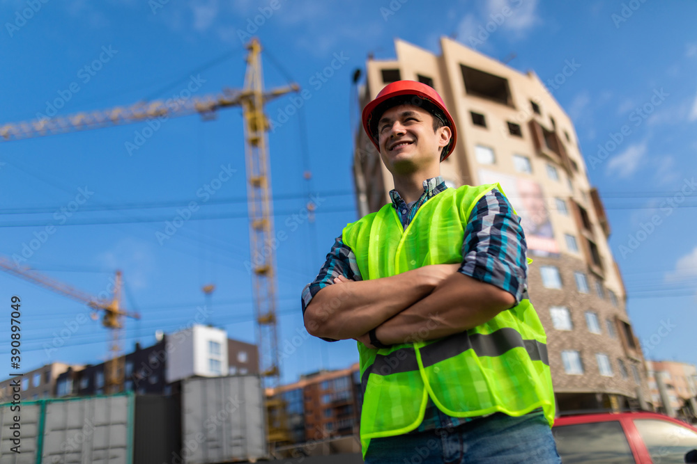 Young engineers man crossed hands at the construction. Young man holding a blueprint and looking at it with inspiration. Young engineers man crossed hands at the construction. Young man holding a blueprint and looking at it with inspiration.