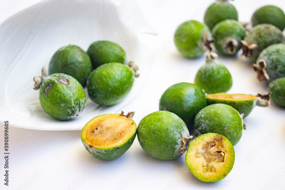 Large fleshy juicy Feijoa berries. Ripe dark green with sepals. A scattering of fruit on a light table and a white Cup. Whole and cut slices. Large fleshy juicy Feijoa berries. Ripe dark green with sepals. A scattering of fruit on a light table and a white Cup. Whole and cut slices.