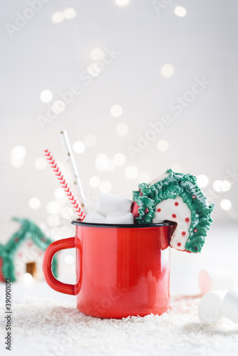 Christmas gingerbread house on a red enamel mug with a hot drink with marshmallows. Selective focus