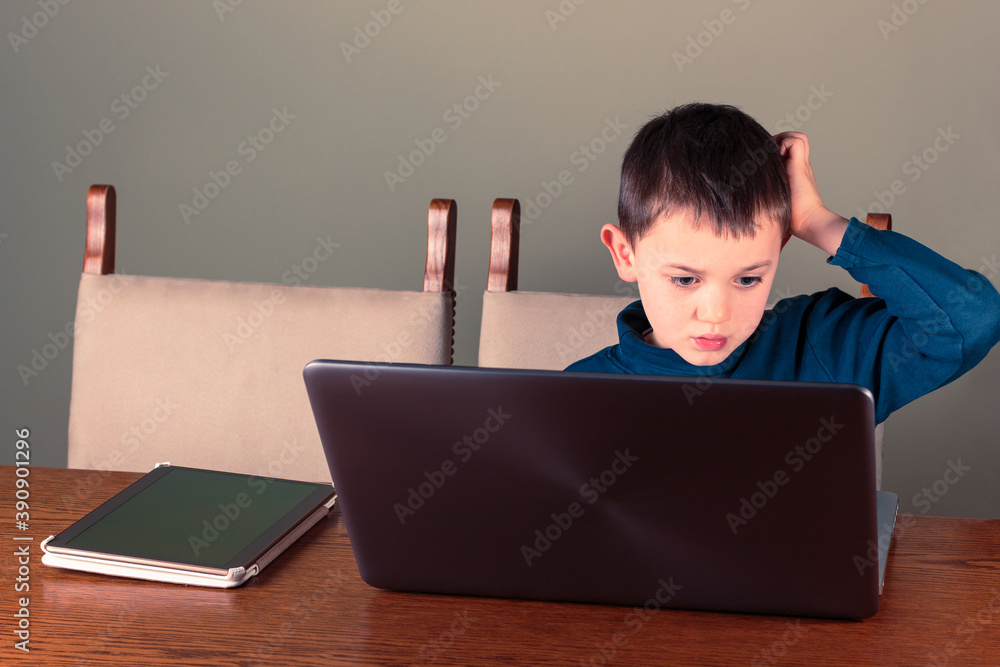 Fotografie Eight year old boy using laptop and tablet computers scratches his head