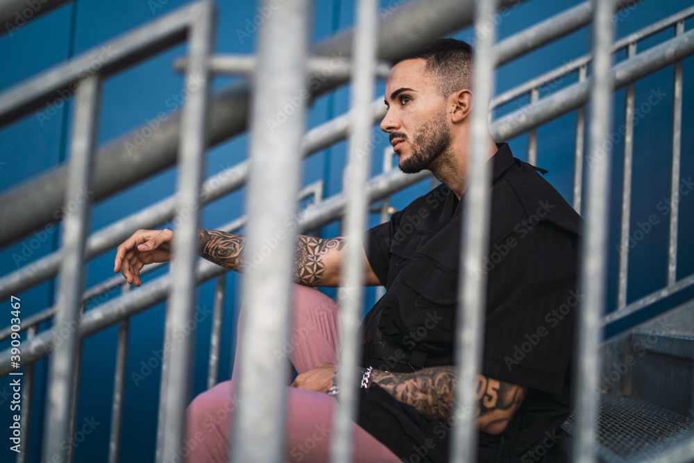 Εκτύπωση καμβά Young hot man wearing a black oversize shirt and pink pants sitting on a stairca